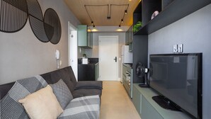 A modern kitchen with a built-in stove, a large flat-screen TV, and a dining area with a dark-colored sofa and patterned cushions. - Laguna 430 (São Paulo)