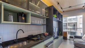 A modern kitchen with a black countertop, stainless steel sink, and a built-in oven. There is a window providing natural light and a view of the outside. - Laguna 430 (São Paulo)