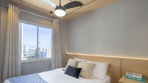 A hotel room with a large bed, a nightstand, a ceiling fan, and a view of the city through a window. - Laguna 430 (São Paulo)