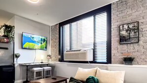 Ein modernes Wohnzimmer mit einer Ledersofa, einem an der Wand montierten Fernseher, einer Ziegelwand und einem Fenster mit Jalousien.