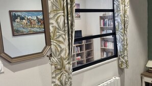 Een slaapkamer met een bed, een radiator, een houten stoel, een boekenplank en een raam met gordijnen.
