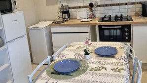 Een compacte keuken met witte apparaten, een eettafel met blauwe borden en een betegelde spatwand.