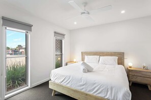 A bedroom with a bed, a ceiling fan, a nightstand, and a window with a view of the outside. - Golf Course Front Stylish Townhouse w/ Pool Access (Cowes)