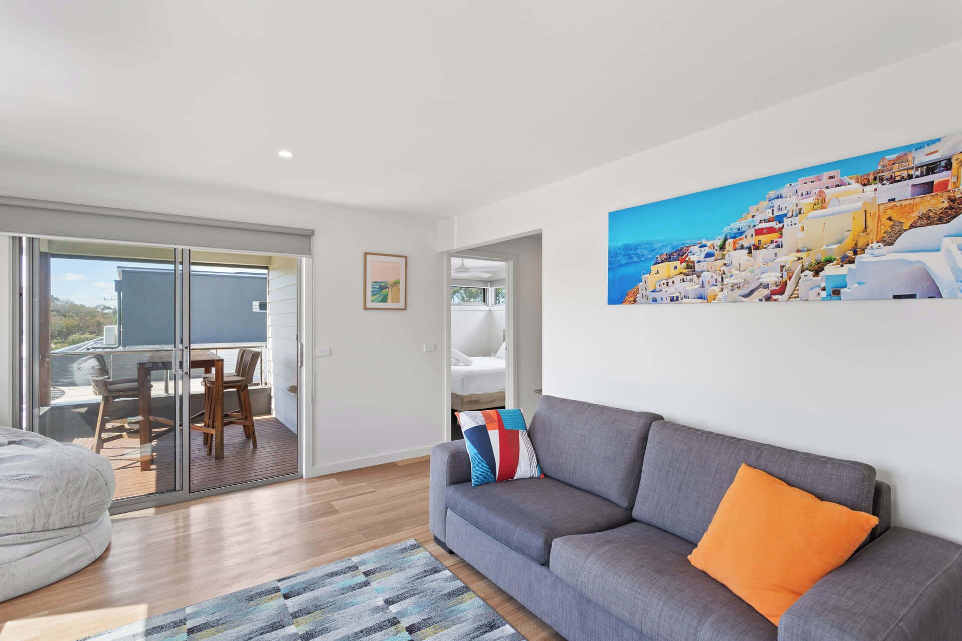 A modern living room with a grey sofa, a colorful rug, and a painting of a coastal town.
