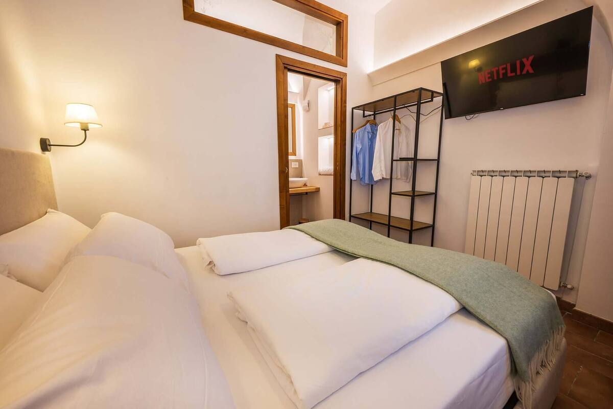 A hotel room with a bed, a wall-mounted Netflix sign, a radiator, and a clothing rack.