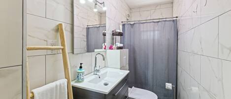 A bathroom with a sink, mirror, towel rack, shower curtain, and toilet.