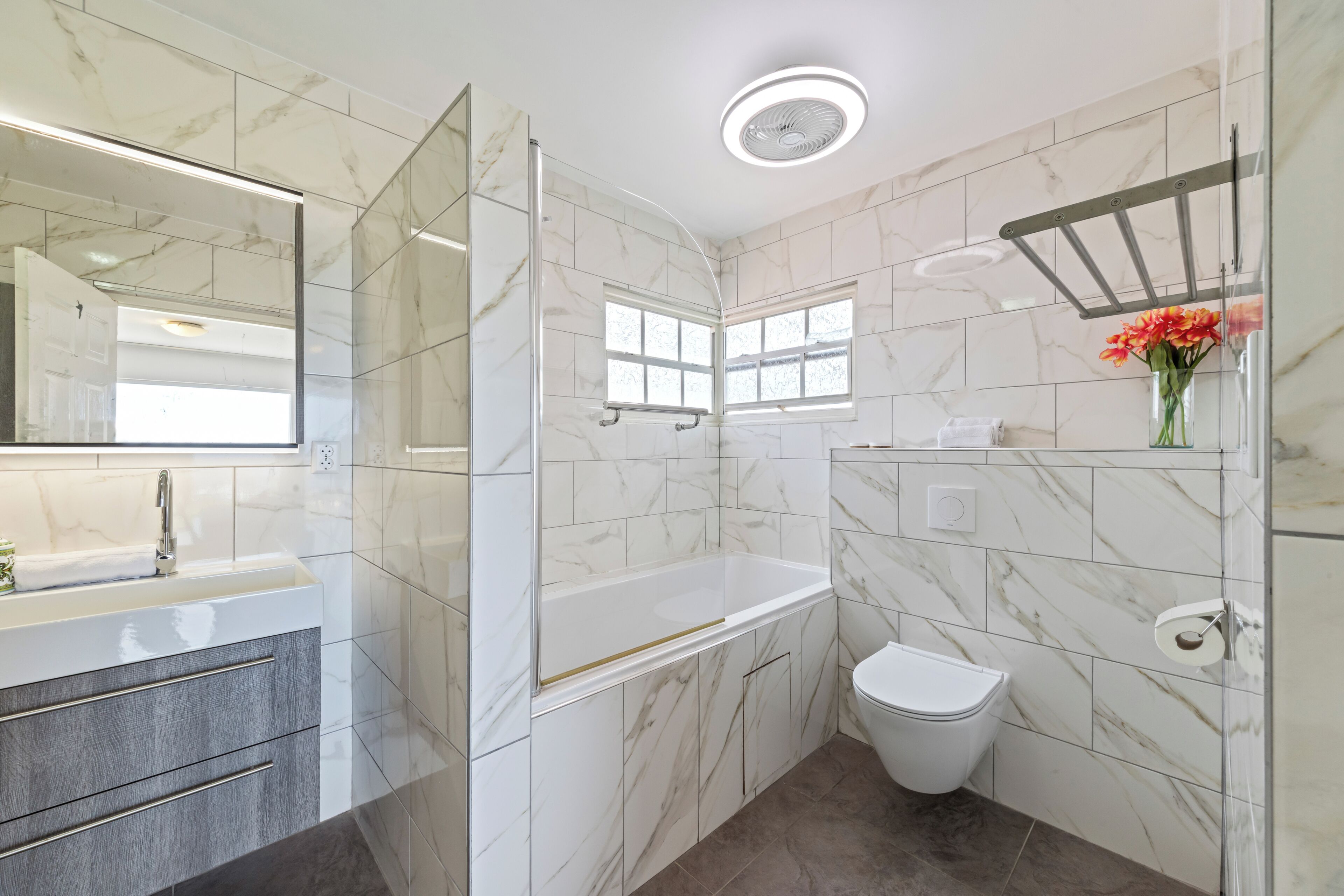 A modern bathroom with a marble tile wall, a glass shower enclosure, a white toilet, and a vanity with a mirror.