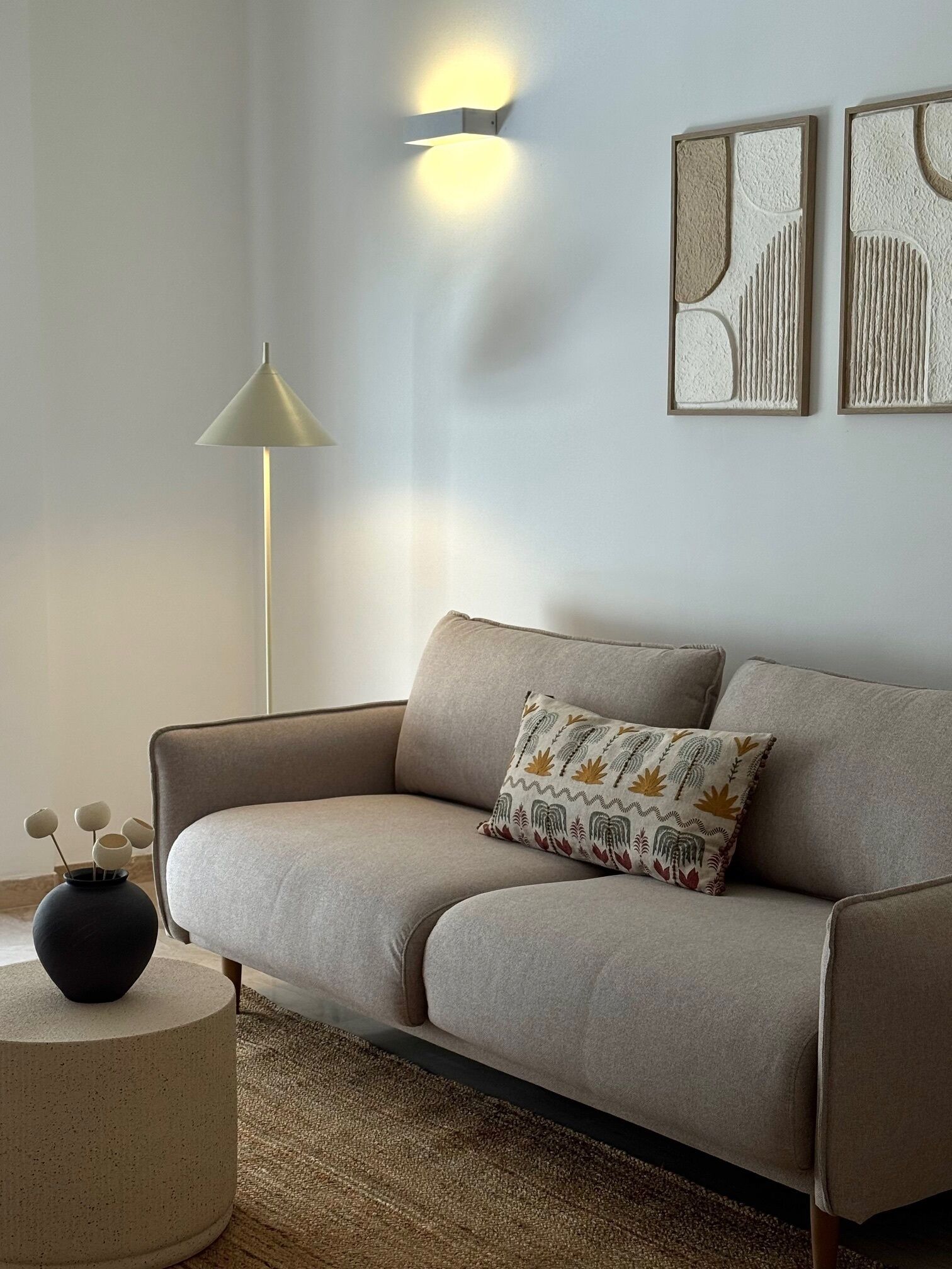Ein modernes Wohnzimmer mit einem beigen Sofa, einem runden Beistelltisch, einer Stehlampe und Wandleuchten.