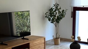 Moderni olohuone, jossa on puinen TV-taso, ruukussa oleva kasvi, pyöreä pöytä maljakolla ja suuri ikkuna, josta avautuu näkymä vehreään maisemaan.