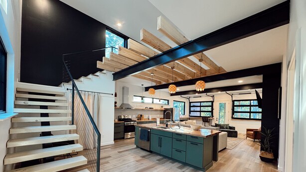 Una cucina moderna con isola centrale, scala in legno e travi a vista.