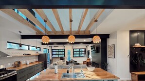 Una cucina moderna con isola centrale, travi in legno, luci a sospensione e vista all'esterno.