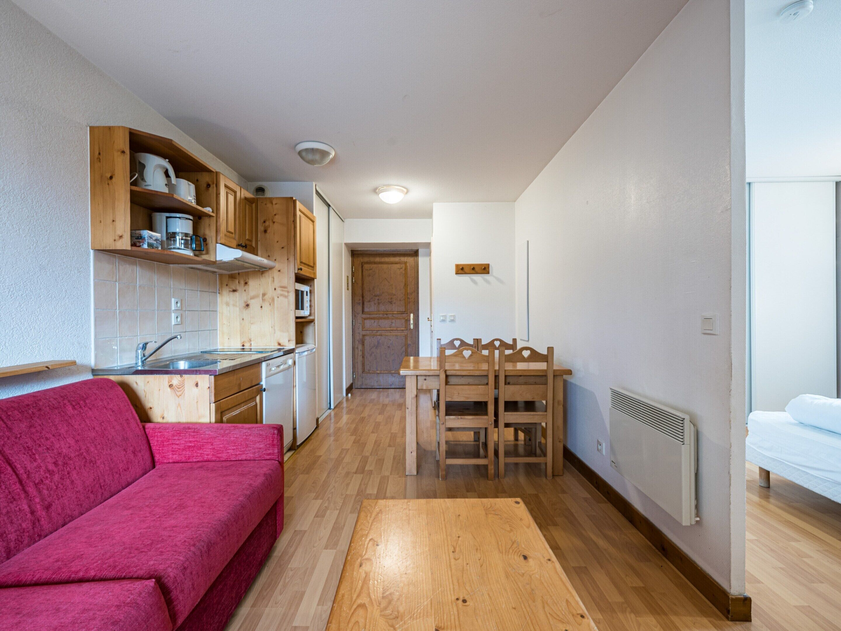 Een kleine keuken met houten kastjes en een eethoek met een tafel en stoelen.