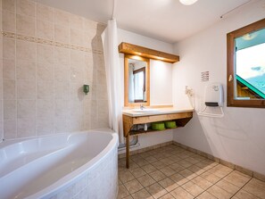 A bathroom with a bathtub, a sink, a mirror, and a window with a view of the sea. - Cosy Apartment in the Mountains in Giez (Giez)