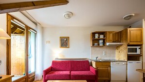 A compact kitchen with wooden cabinets, a red sofa, and a wooden table. - Cosy Apartment in the Mountains in Giez (Giez)