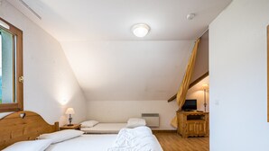 A bedroom with two beds, a wooden headboard, a bedside table with a lamp, a TV on a wooden cabinet, and a window with curtains. - Cosy Apartment in the Mountains in Giez (Giez)