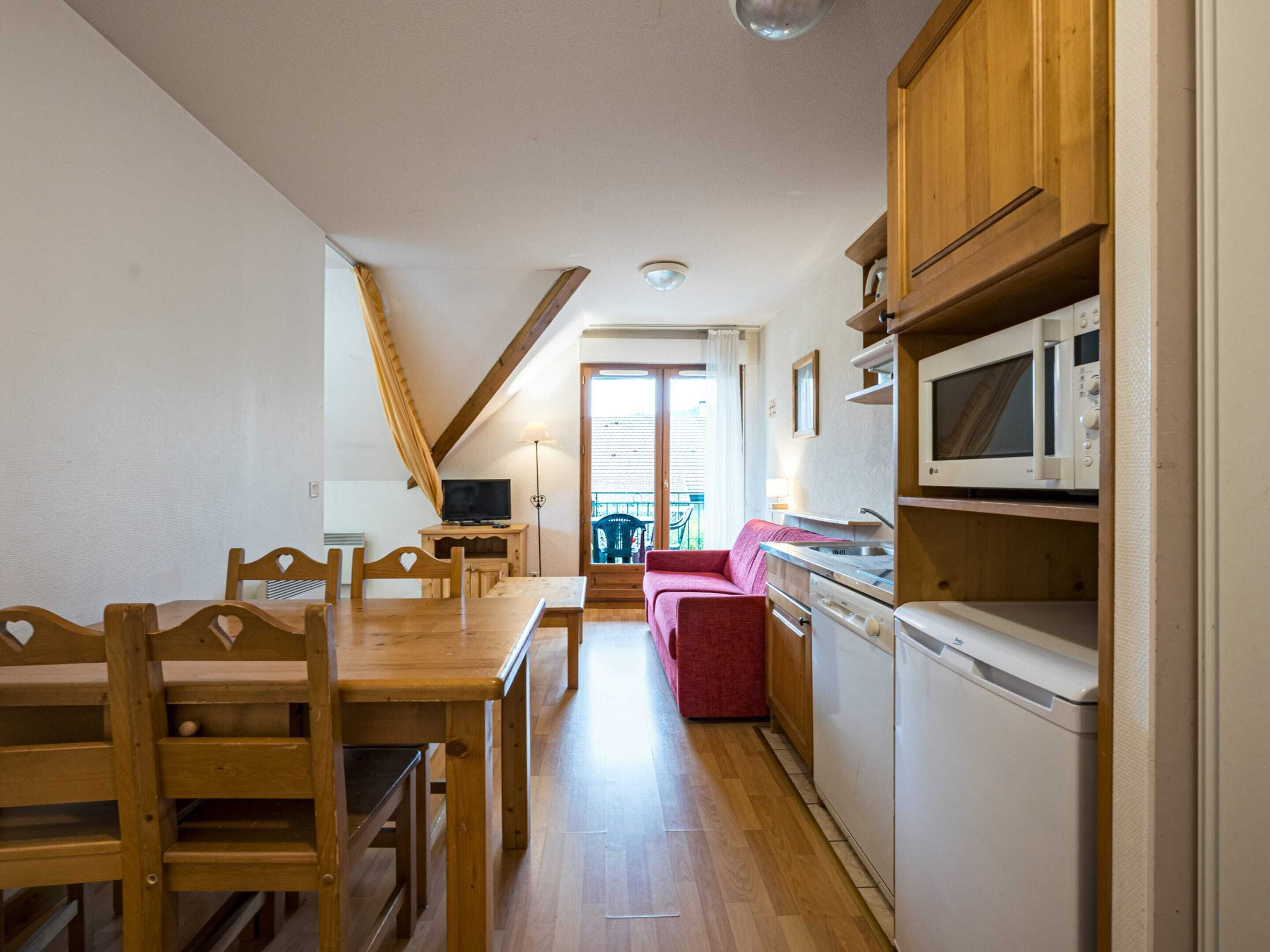 Cocina compacta con armarios de madera, microondas y zona de comedor con mesa y sillas.