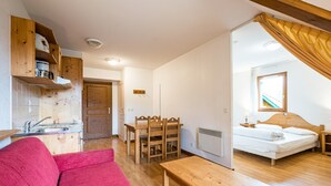 A compact living space with a kitchenette, a dining area, a bed, and a red sofa. - Cosy Apartment in the Mountains in Giez (Giez)