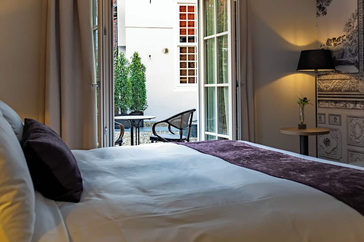 Une chambre d’hôtel avec un lit, une petite table avec des chaises, une plante en pot et une vue sur l’extérieur.