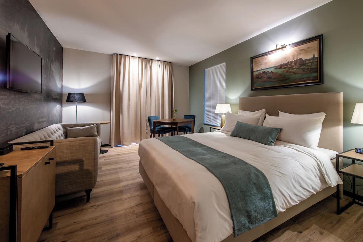 Une chambre d’hôtel avec un grand lit, un bureau, une chaise, une télévision et un tableau au mur.