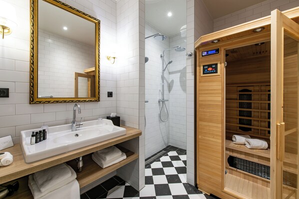Un baño moderno con lavamanos, espejo y ducha blancos. Incluye una sauna de madera y estantes con toallas.