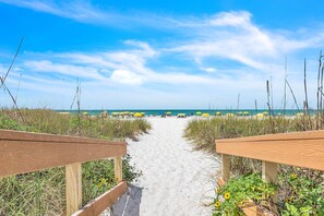 A beach path leading to the ocean with beach umbrellas and a wooden fence. - Sunset Vistas 403S🌞Beach Access Onsite🌴Large Heated Pool/Hot Tub (Treasure Island)