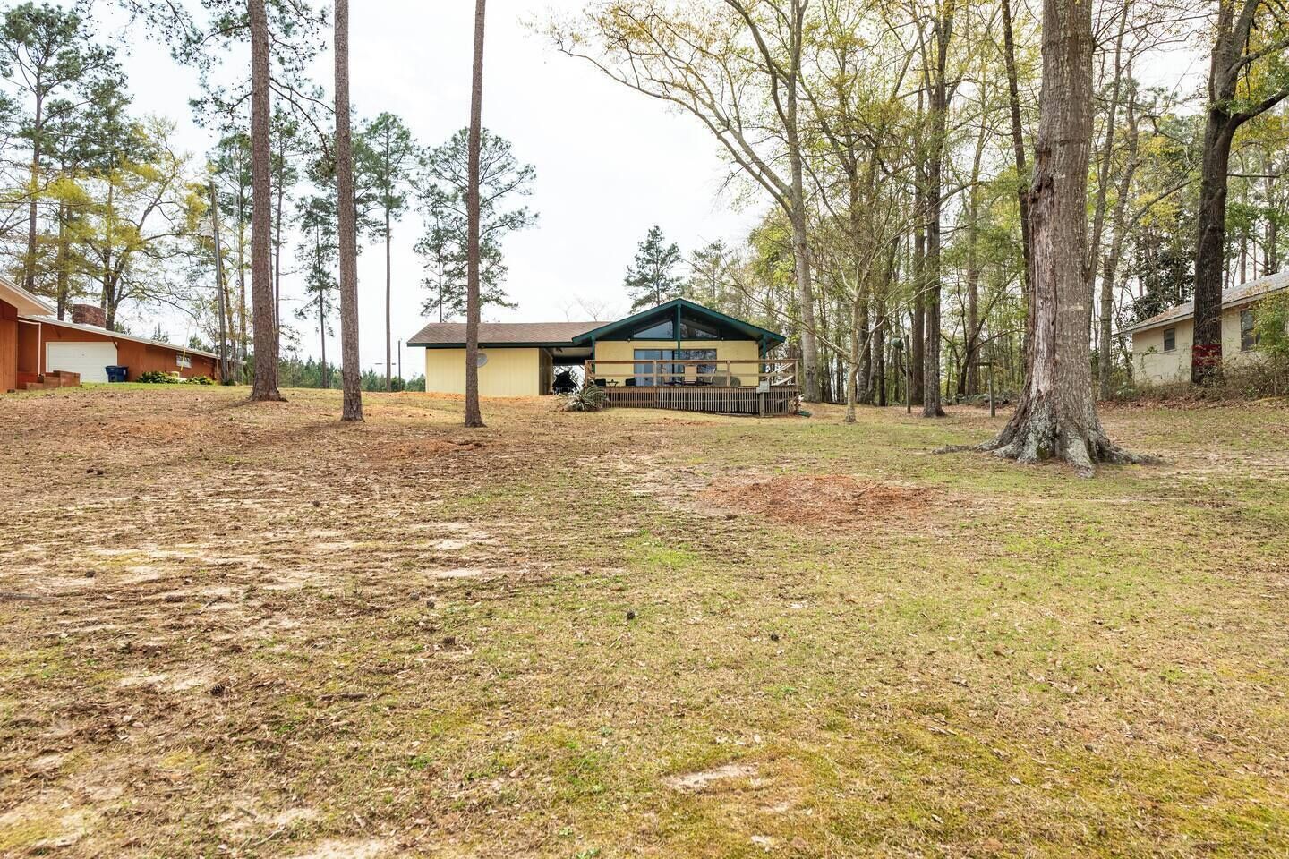 A single-story house with a green roof, surrounded by trees and a grassy yard.