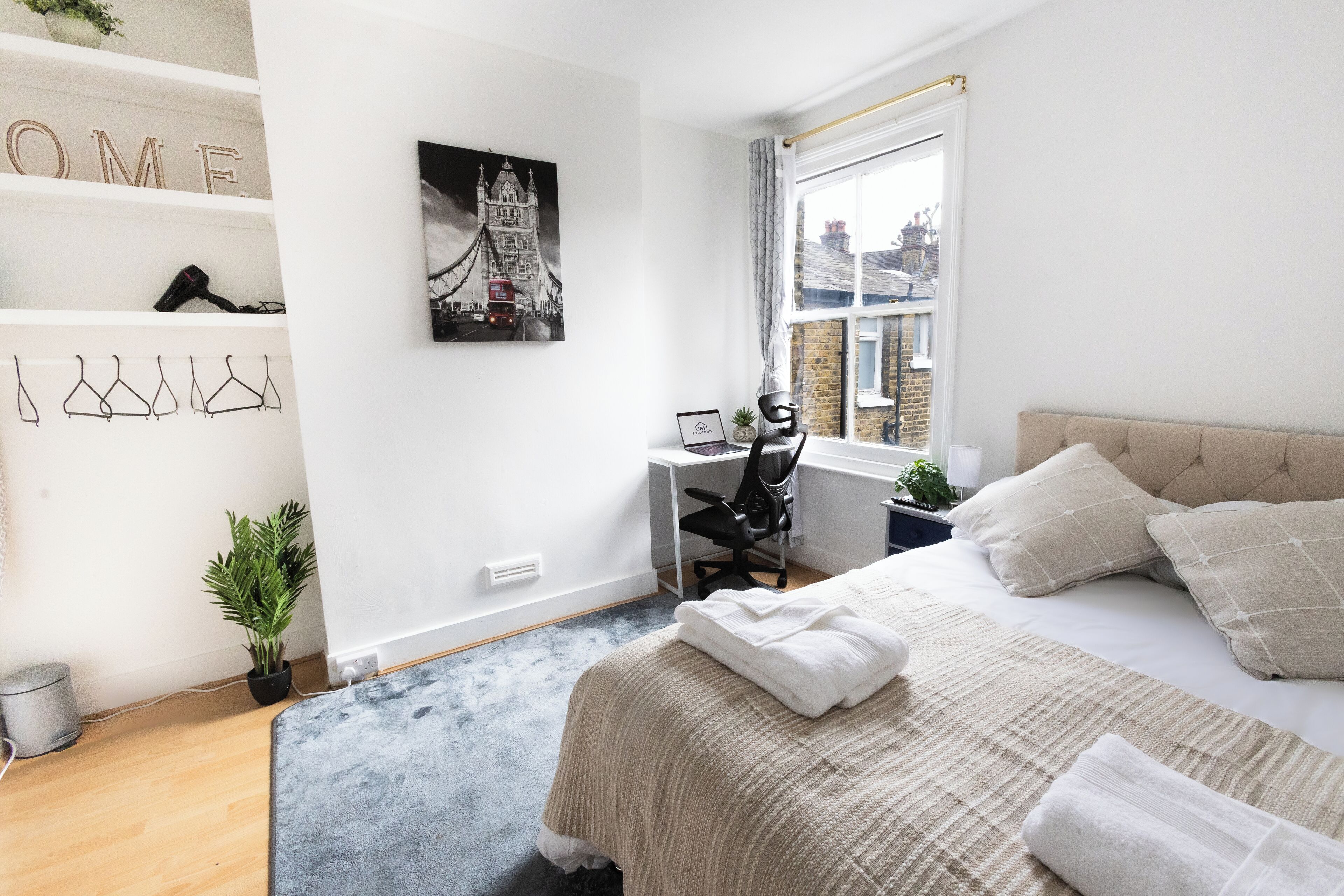 Un dormitorio con cama, escritorio, silla y ventana con vistas a edificios.