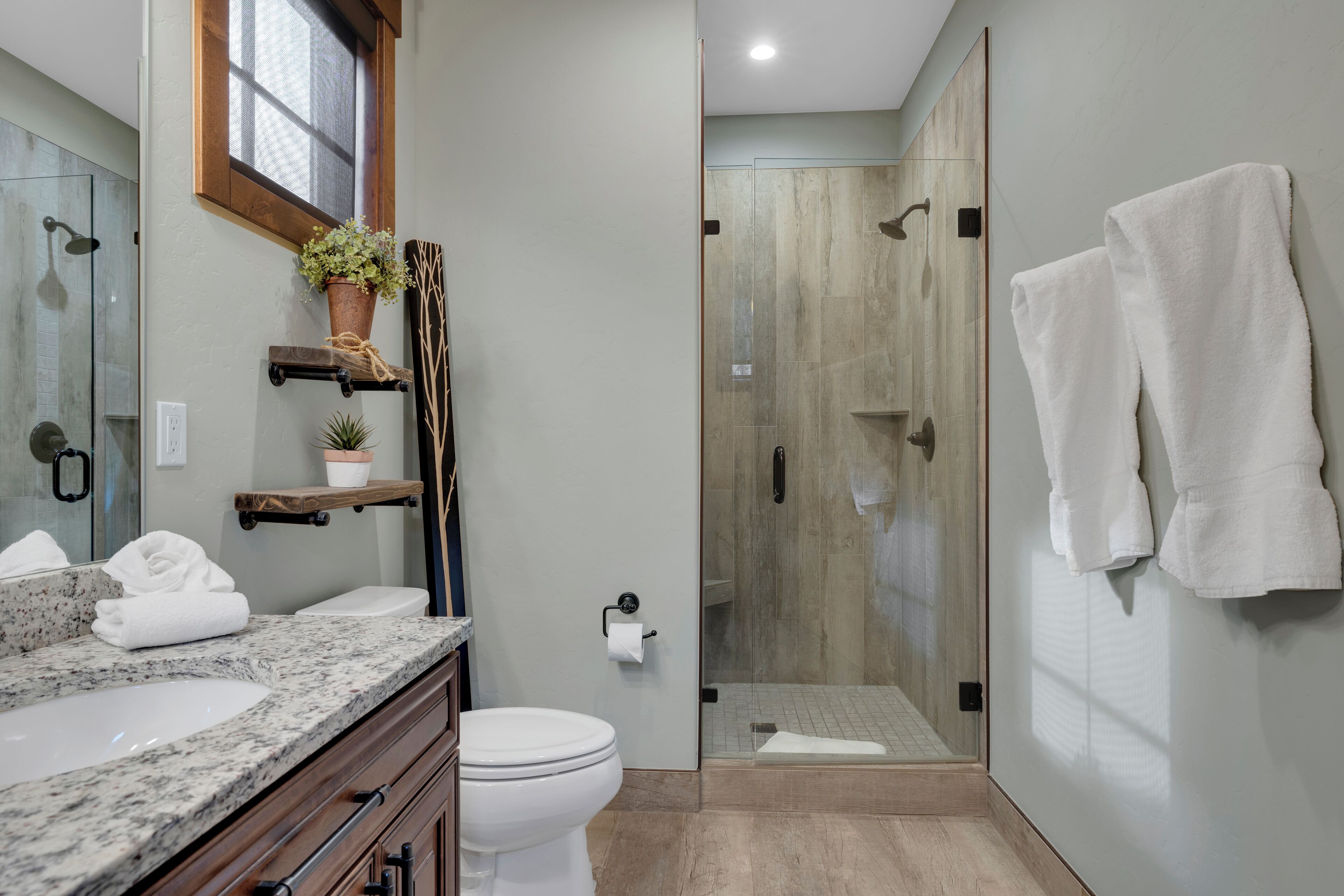 A modern bathroom with a granite countertop, a white toilet, a glass shower enclosure, and a towel rack with two towels.
