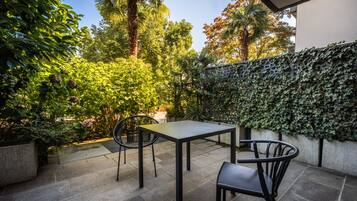 Un patio exterior con mesa y sillas, rodeado de abundante vegetación y un muro decorativo.