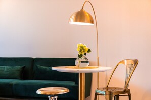 A modern living room with a green sofa, a round table with a vase of flowers, a floor lamp, and a chair.