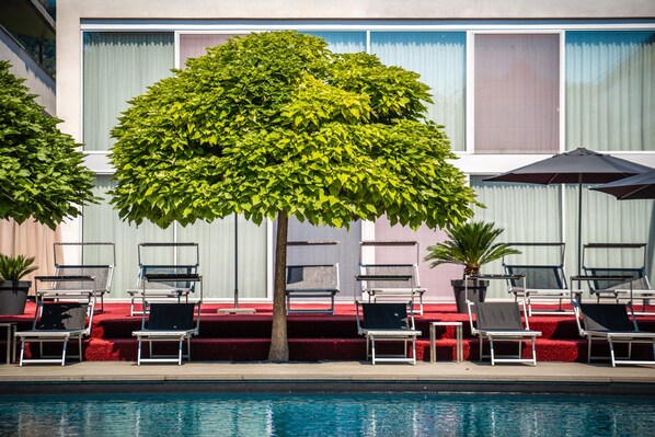 A poolside area with lounge chairs and a tree.
