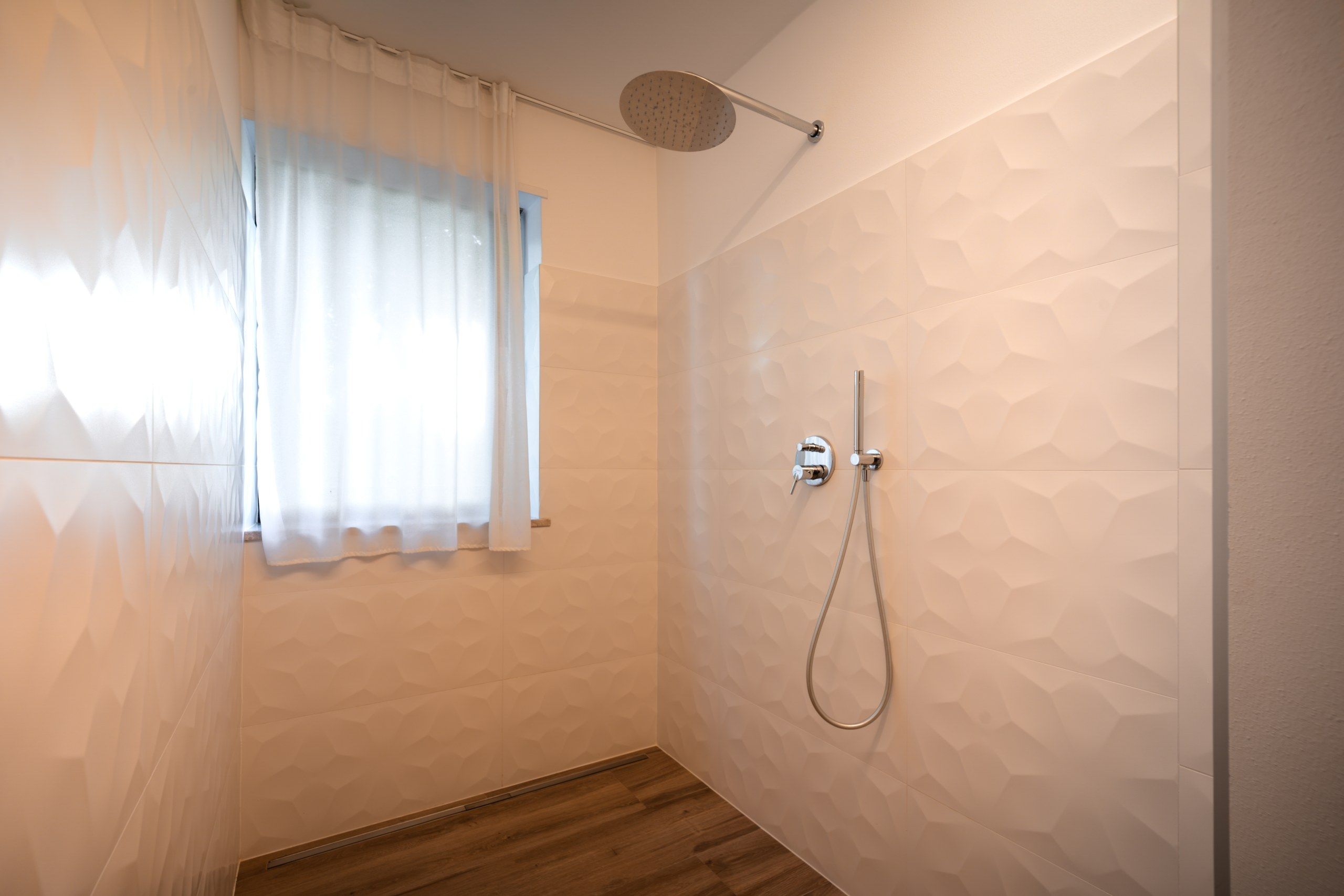 Un baño con ducha, una ventana con cortinas y piso de madera.