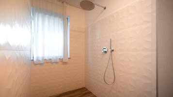 Un baño con ducha, una ventana con cortinas y piso de madera.