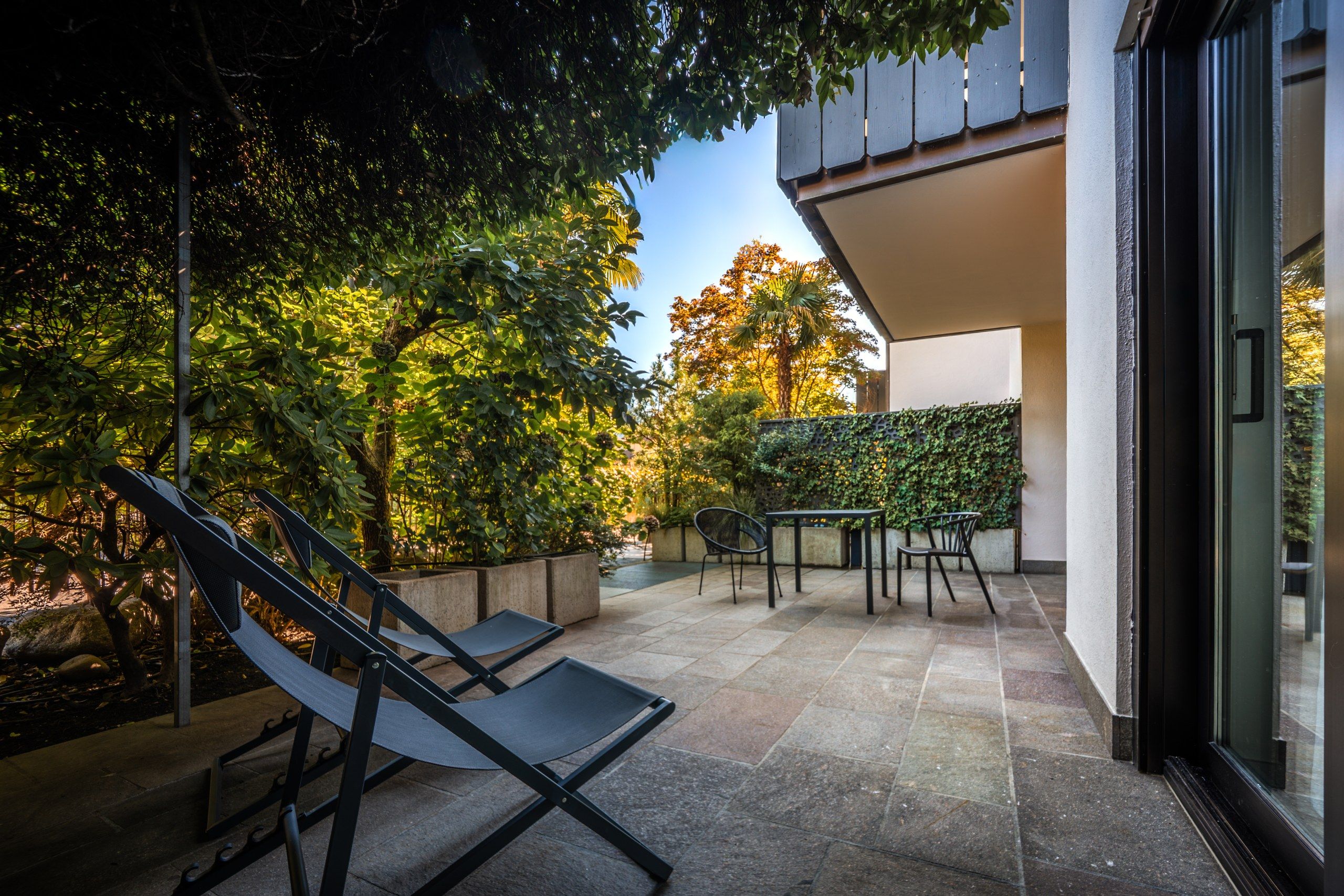 A patio with outdoor furniture, a wall with climbing plants, and a view of trees.