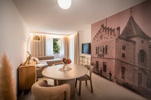 A modern hotel room with a round dining table, a sofa, and a large mural of a historic building. - 739B goldfinger+suites I Apartment Individual 3 (Lana)