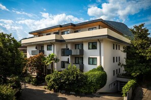 Ein modernes, mehrgeschossiges Gebäude mit Balkonen, umgeben von Grünflächen und mit Blick auf einen Berg.
