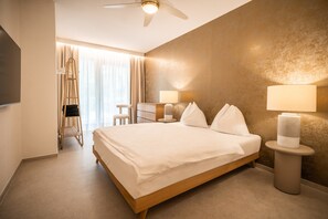 A hotel room with a large bed, bedside lamps, a desk, and a chair. - 739B goldfinger+suites I Apartment Individual 3 (Lana)