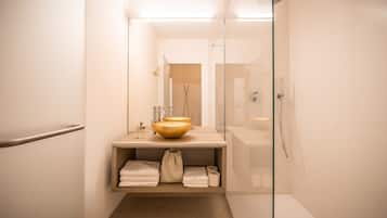 Ein Badezimmer mit einer Duschkabine, einem beige gefärbten Waschbecken mit goldener Schüssel und einem Handtuchhalter.