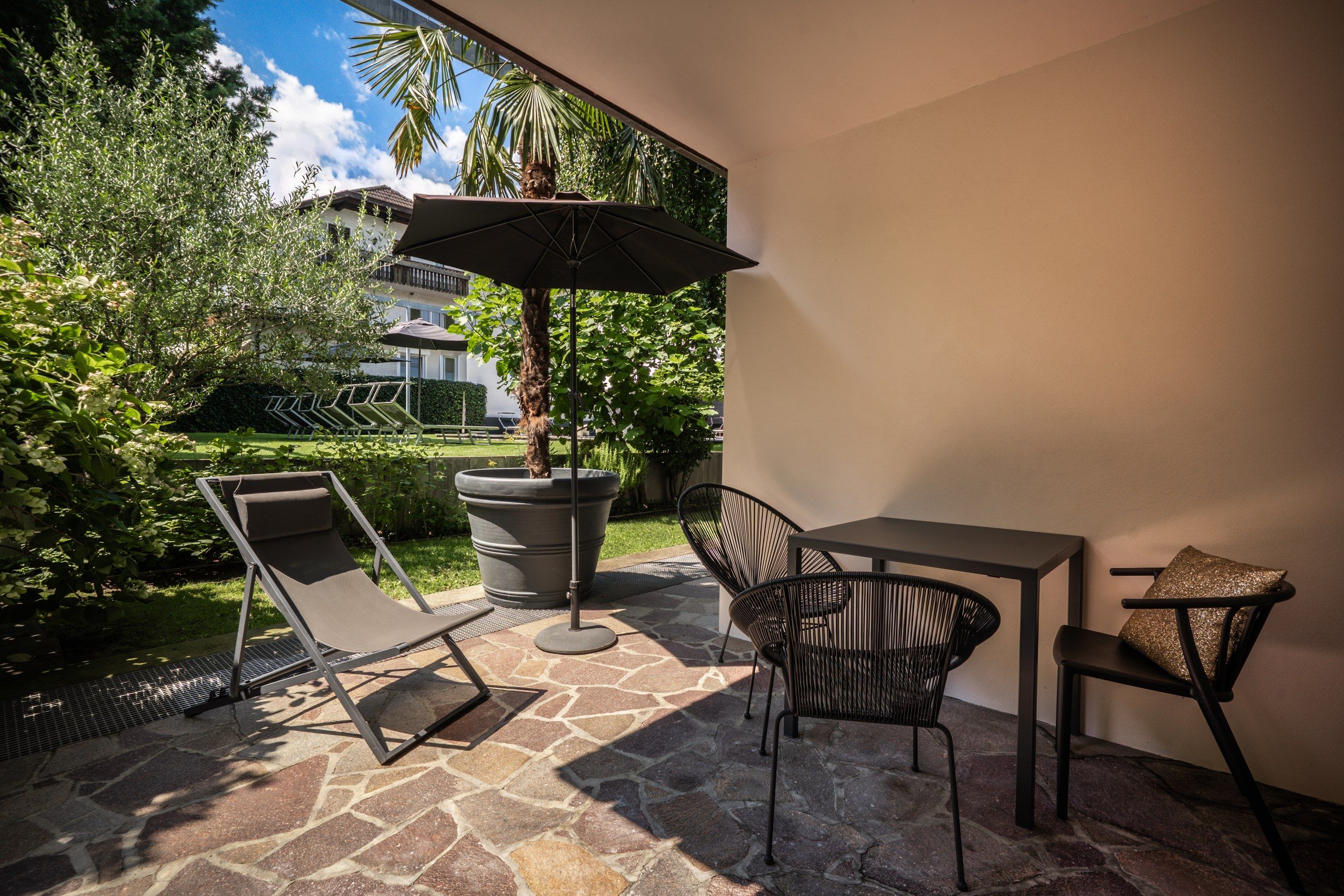 Une terrasse extérieure avec une table et des chaises, un grand bac à fleurs et un parasol.