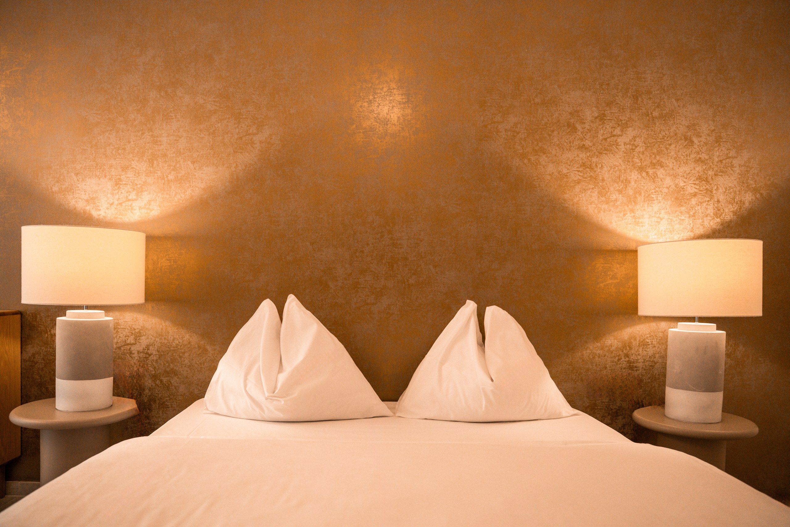 Een hotelkamer met een gestructureerde muur, twee bedlampen en een bed met wit beddengoed.
