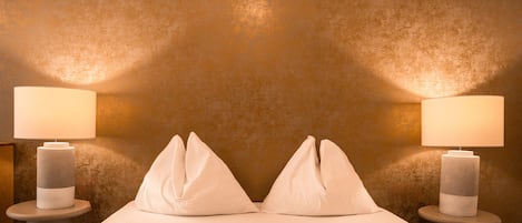 A hotel room with a textured wall, two bedside lamps, and a bed with white bedding.