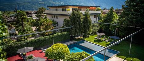 Um hotel moderno com piscina, cercado por vegetação exuberante e montanhas ao fundo.