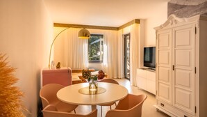 Et moderne hotelværelse med et rundt spisebord, lyserøde stole, et hvidt skab og et fjernsyn.