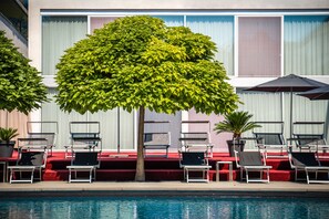 Un espace aménagé au bord de la piscine, avec des chaises longues et un arbre.
