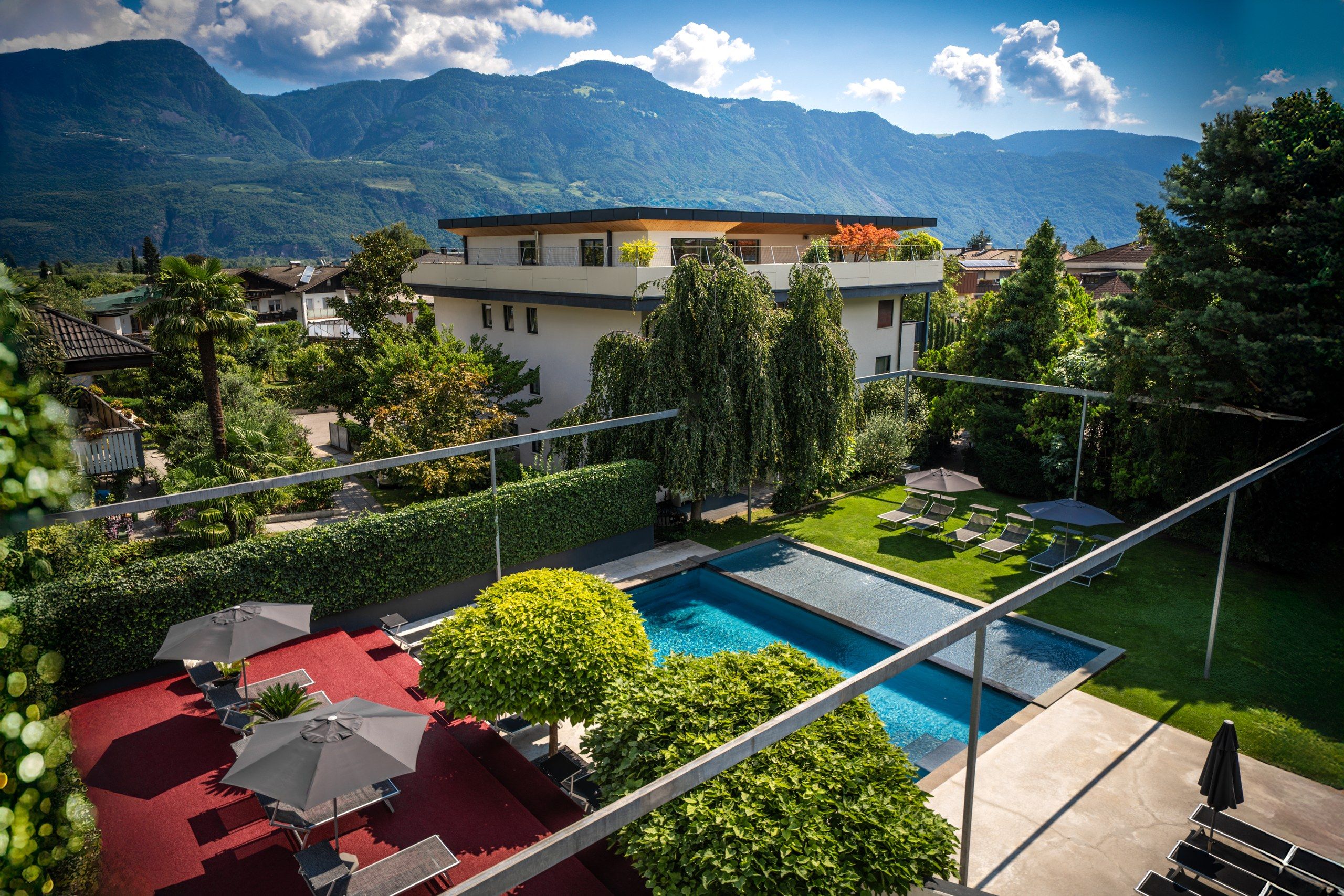 A modern hotel with a swimming pool, surrounded by lush greenery and mountains in the background.