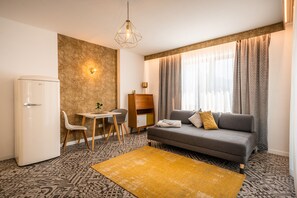 A compact living space with a sofa, a dining table with chairs, a small cabinet, and a refrigerator.