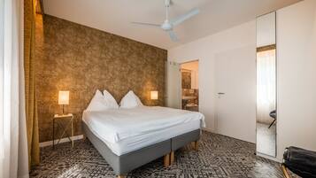Una camera d'hotel con un letto, una ventola a soffitto, un pavimento decorato e un bagno visibile attraverso una porta aperta.