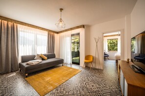 A modern living room with a sofa, a yellow rug, and a dining area with a table and chairs. - 739F Goldfinger+Suites I Apartment Unique 15 (Lana)