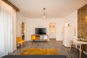 A modern living room with a flat-screen TV, a yellow chair, a dining table, and a patterned rug. - 739F Goldfinger+Suites I Apartment Unique 15 (Lana)