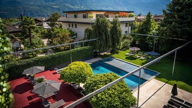 A modern hotel with a swimming pool, surrounded by lush greenery and mountains in the background. - 739F goldfinger+suites I Apartment Unique 15 (Lana)